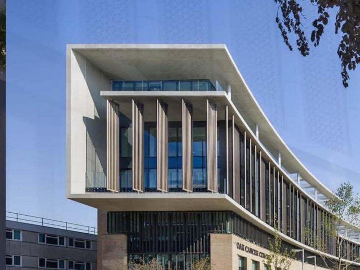 A projecting stone-clad soffit and roof canopy with a run of aluminium louvres on a completed building elevation, under a clear sky.