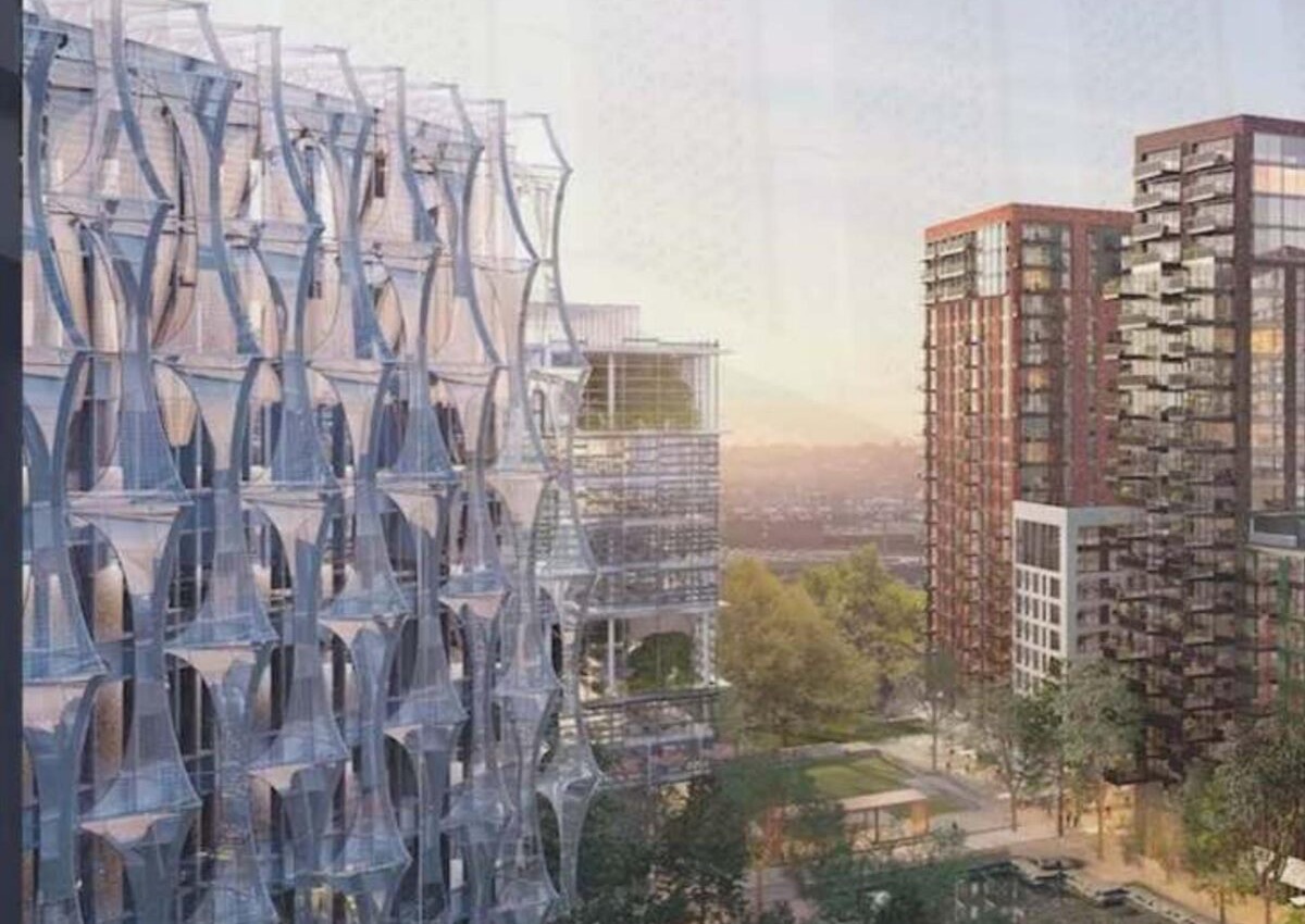 A structural glazing screen with tensioned cable and steel supports on a building elevation, residential tower blocks visible beyond under a hazy sky.